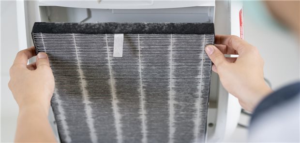 Eine Frau wechselt den verschmutzten Filter des Luftreinigers nach längerem Gebrauch in einer verschmutzten Umgebung.