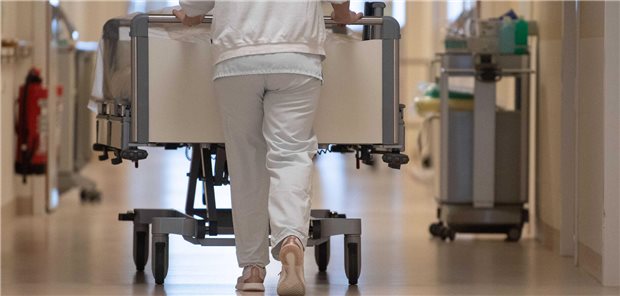 Eine Pflegekraft schiebt ein Krankenbett über die Station eines Krankenhauses.