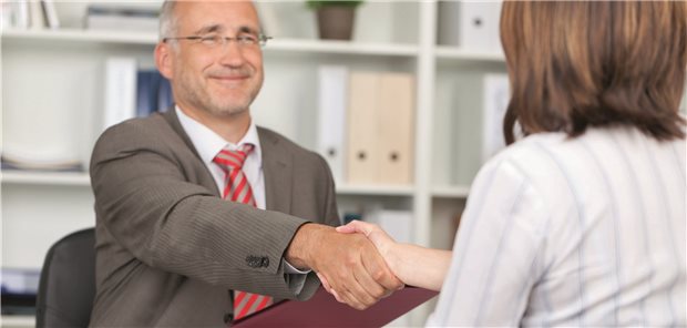 Private Zusatzversicherungen vom Arbeitgeber immer beliebter Vertragsabschluss? Ein Mann im Anzug mit einer roten Mappe in der Hand reicht einer Dame in heller Bluse (von hinten im Bild) die Hand.
