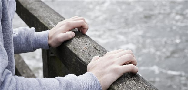 Hände, die sich an der Brüstung einer Brücke über einem Fluss festkrallen.