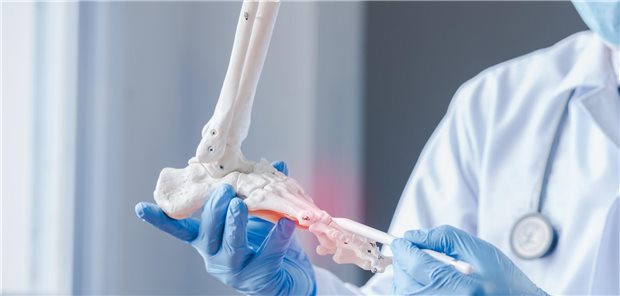 Ein Orthopäde erklärt am Modell eines Fußes einem Patienten die Diagnose und den Behandlungsplan.