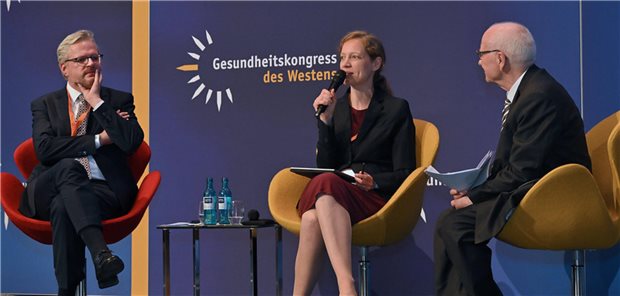 Amelie Wuppermann sitzt auf einem Podium zwischen zwei anderen Diskutanten und spricht ins Mikrofon.