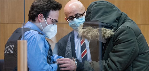 Syrischer Arzt soll in 18 Fällen gefoltert haben Prozessauftakt: Dem aus Syrien stammenden angeklagten 36-jährigen Arzt werden im Sicherheitssaal des OLG Frankfurt am Main die Handschellen abgenommen. In der Bildmitte sein Anwalt Oussama Al-Agi.