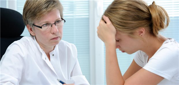 Frau im weißen Kittel schaut Mädchen an, das sich Hand vor die Stirn hält