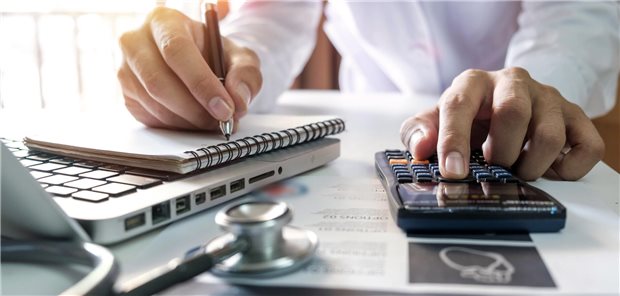 Arzt sitzt am Schreibtisch und tippt in einen Taschenrechner