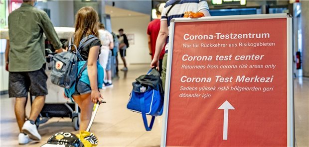 Coronavirus in Hamburger Heime und Kliniken eingeschleppt Reisende gehen aus dem Sicherheitsbereich des Hamburger Flughafens an einem Schild vorbei, das auf das Corona-Testzentrum verweist: Nach wie vor sind Reiserückkehrer eine Quelle für Neuinfektionen (Archivfoto vom August).