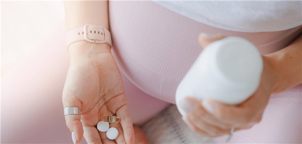 Nahaufnahme von zwei weißen runden Pillen in der Hand einer jungen schwangeren Frau.