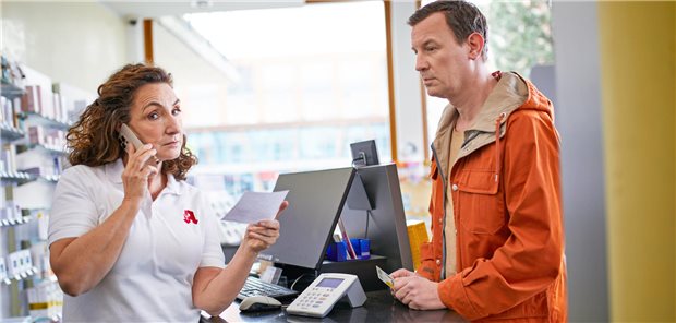 Eine Apothekerin steht vor einem Kunden und hat links ein Rezept in der Hand und rechts einen Telefonhörer.