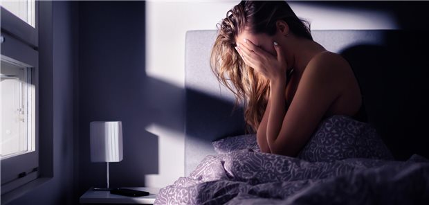 Junge Frau sitzt im Bett und hält sich die Hände ins Gesicht.