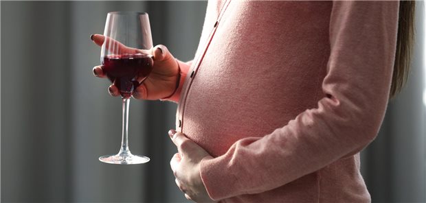 Schwangere Frau mit einem Glas Rotwein in der Hand.