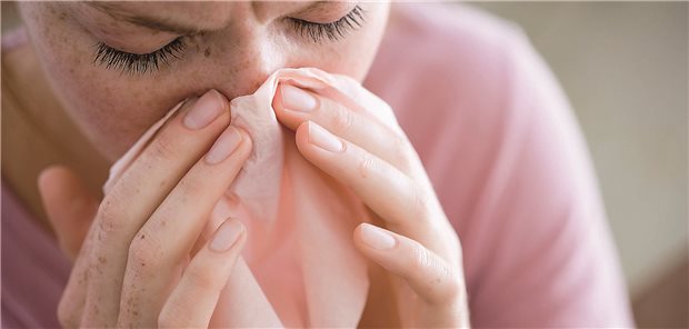 Junge Frau mit Erkältung, die sich die Nase putzt.