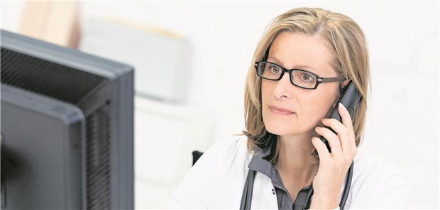 Ärztin mit Telefon am Ohr schaut auf Monitor.