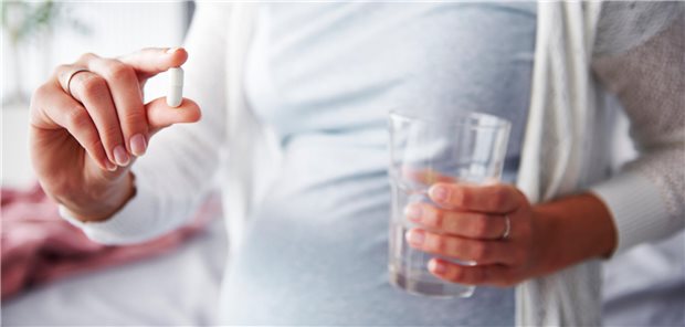 Schwangere Frau mit Glas Wasser und einem Nahrungsergänzungspräparat