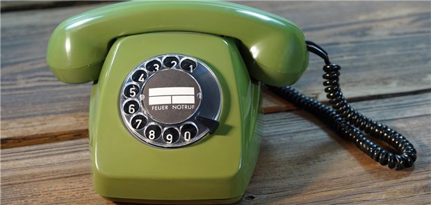 Ein grünes Telefon mit Wählscheibe steht auf einem Holztisch.
