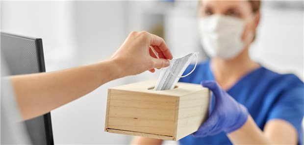 MFA reicht einer Person eine Chirurgen-Maske.