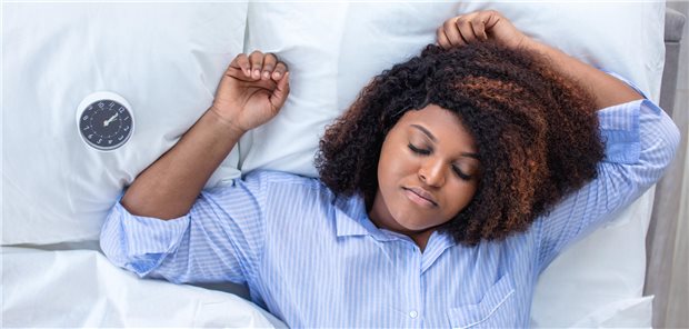 Frau liegt schlafend im Bett, neben ihr liegt ein Wecker