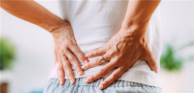 Nahaufnahme einer Frau mit Schmerzen im unteren Rückenbereich.