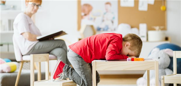 Stigma ADHS: Wer denkt was über wen? Kind mit ADHS sitzt an einem Tisch und hat seinen Kopf auf den Tisch gelegt.