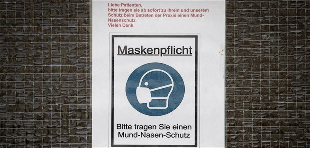 Auf der Eingangstür einer Arztpraxis wird auf die Maskenpflicht hingewiesen.