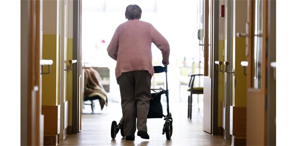 Eine ältere Dame schiebt einen Rollator über den Flur eines Pflegeheimes.