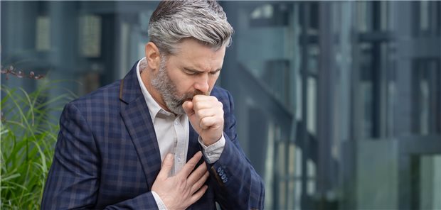 Ein grauhaariger Mann im Anzug hustet. 