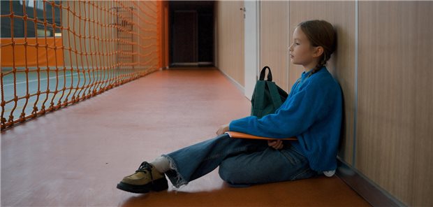 Mädchen sitzt traurig auf dem Boden einer Turnhalle