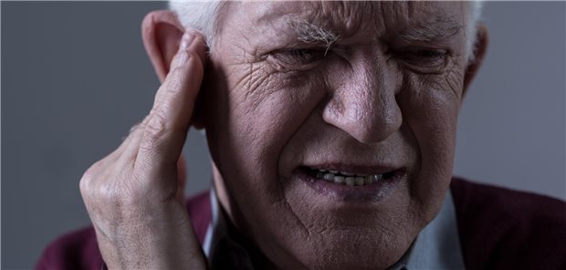 Ein älterer Mann greift sich mit der Hand ans Ohr.