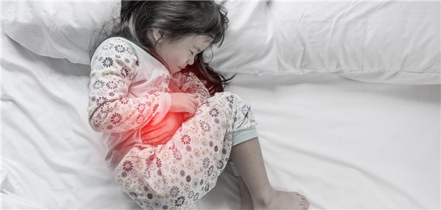 Ein junges Mädchen liegt mit Schmerzen gekrümmt auf einem Bett.