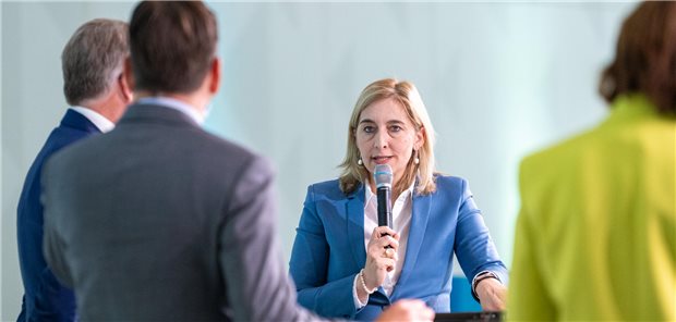 Nina Warken steht auf der Bühne inmitten anderer Diskussionsteilnehmer, die man von hinten sieht.