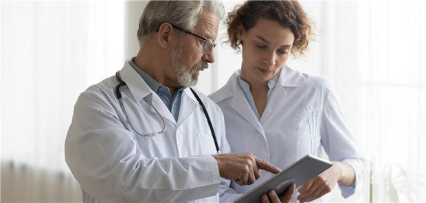 Eine Ärztin und ein Arzt stehen zusammen und schauen gemeinsam auf ein Tablet.