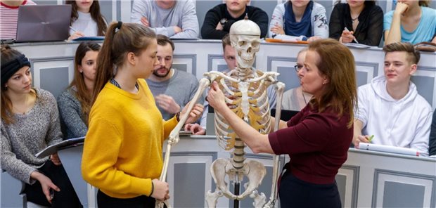 Medizinstudierende schauen einer Dozentin beim Erklären eines menschlichen Skeletts zu.
