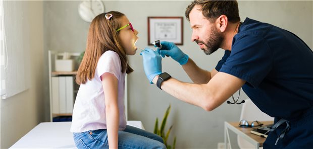 Kinderarzt mit blauen medizinischen Handschuhen untersucht den Rachen eines jungen Patienten mit Halsschmerzen.