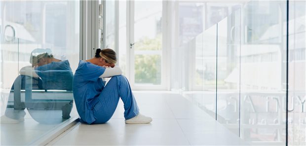 Eine Ärztin sitzt am Boden und hat den Kopf auf ihren Arm gelegt.