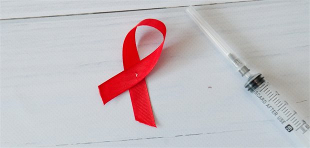Syringe and red ribbon on a light wooden background. World AIDS Day.