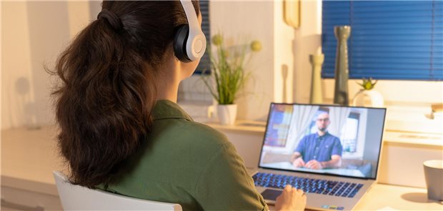 Rückenansicht einer jungen Frau, die an einem Laptop sitzt und Kopfhörer trägt  um an ihrer Video-Fernberatung mit ihrem Psychotherapeuten teilzunehmen.