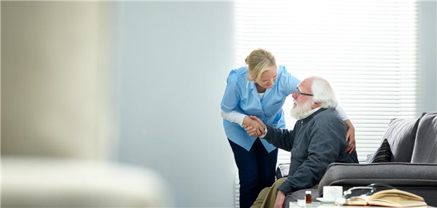 Fachkraft im Heim unterstützt einen pflegebedürftigen Senior.