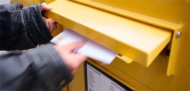 Mann wirft Brief in Briefkasten ein.