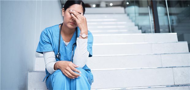 Eien Ärztin sitzt erschöpft auf einer Treppe und hat ihre Stirn in ihre Hand gelehnt.