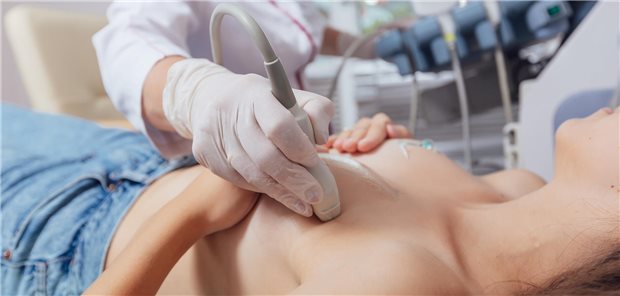 Eine junge Frau liegt auf dem Rücken, während der Arzt ihre Brust ultraschallt.