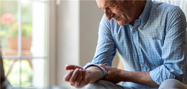 Ein älterer Mann mit rheumatoider Arthritis reibt sich seinen schmerzenden Arm.