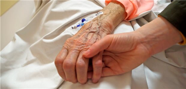 Menschen in häuslicher Pflege: Lebenszeitkalkulator berechnet Sterberisiko jüngere Person hält die Hand einer Älteren, der ein Zugang gelegt wurde.