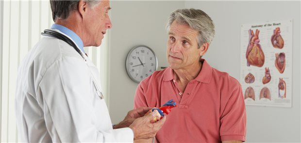 Ein Arzt ist im Gespräch mit seinem Patienten. Der Arzt hält ein Herzmodell in der Hand.