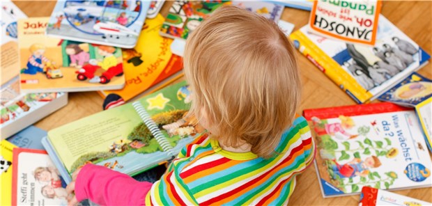 Ein Baby sitzt vor vielen bunten Bilderbücher