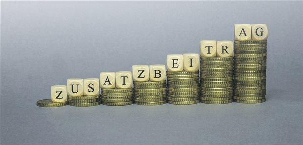 Würfel, die das Wort Zusatzbeitrag bilden, liegen auf Euromünzen.