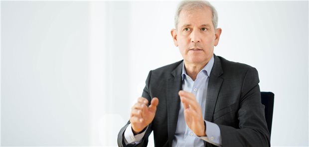 Uniklinika-Chef Professor Jens Scholz sitzt auf einem Stuhl und hält seine Hände mit erklärender Gestik vor der Brust.