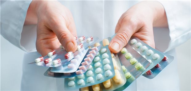 Person im Kittel hält eine Vielzahl von Blistern verschiedener Tabletten in den Händen. 