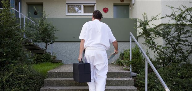 Arzt mit Koffer geht Treppen zu einem Haus hoch.
