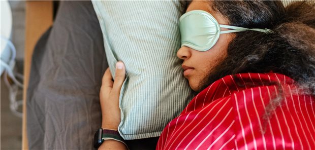 Eine junge Frau trägt eine Schlafmaske und liegt im Bett.
