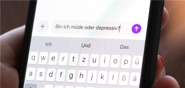 Eine Person hält ein Smartphone in der Hand, auf dem eine Suchanfrage mit der Frage „Bin ich müde oder depressiv?“ in einem KI-Chatfenster zu sehen ist.