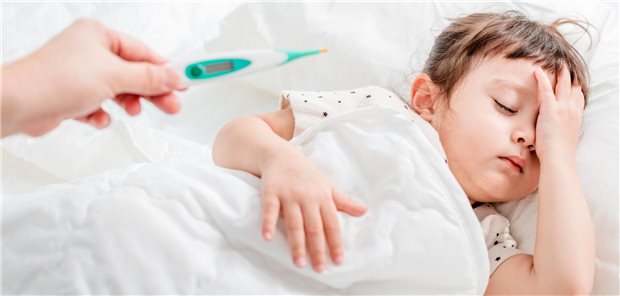 Mädchen sitzt mit einer Wärmflasche und einer Decke im Bett.